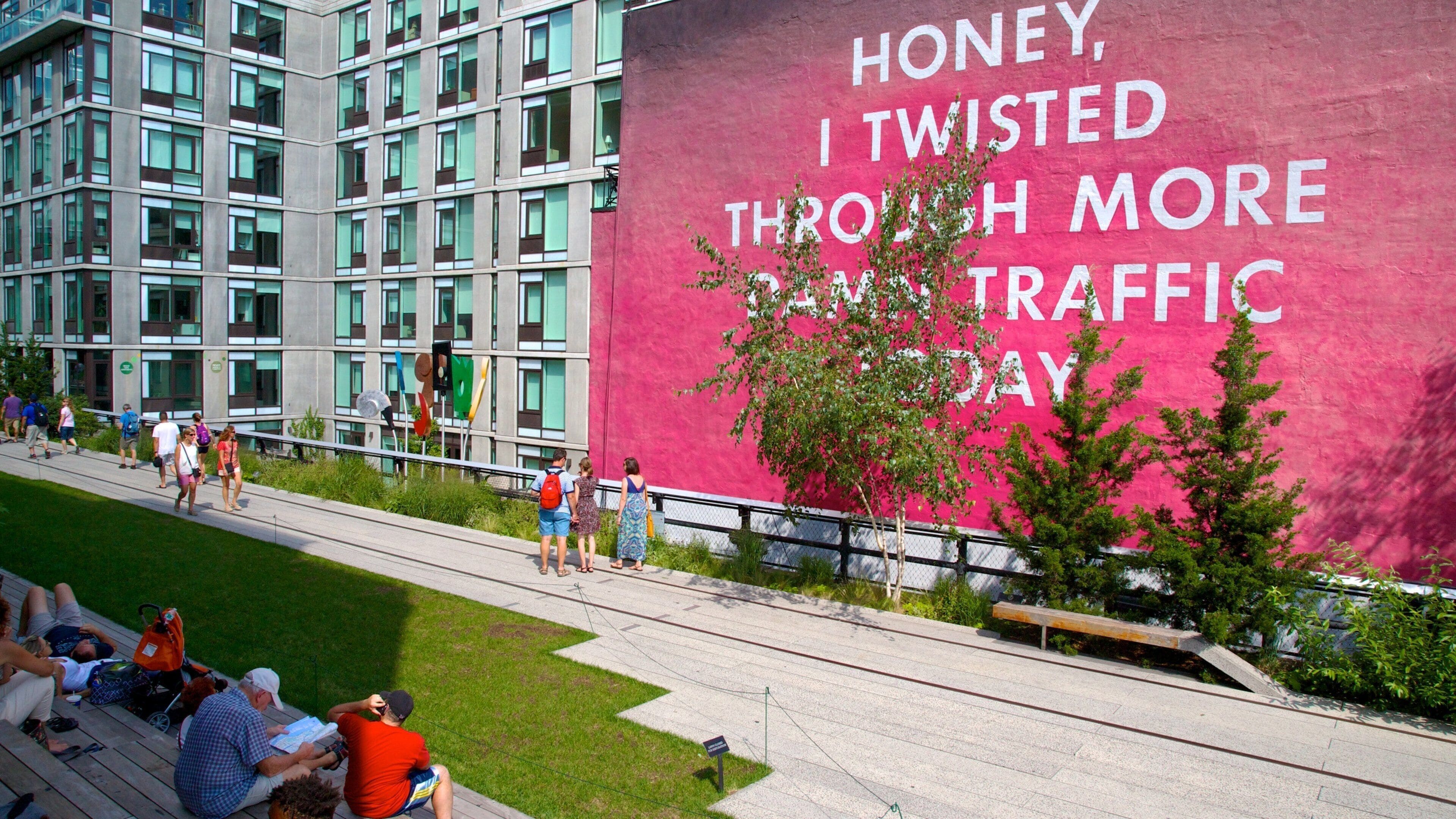 Un mur rose avec du texte blanc, une zone herbeuse et un bâtiment moderne doté de nombreuses fenêtres.