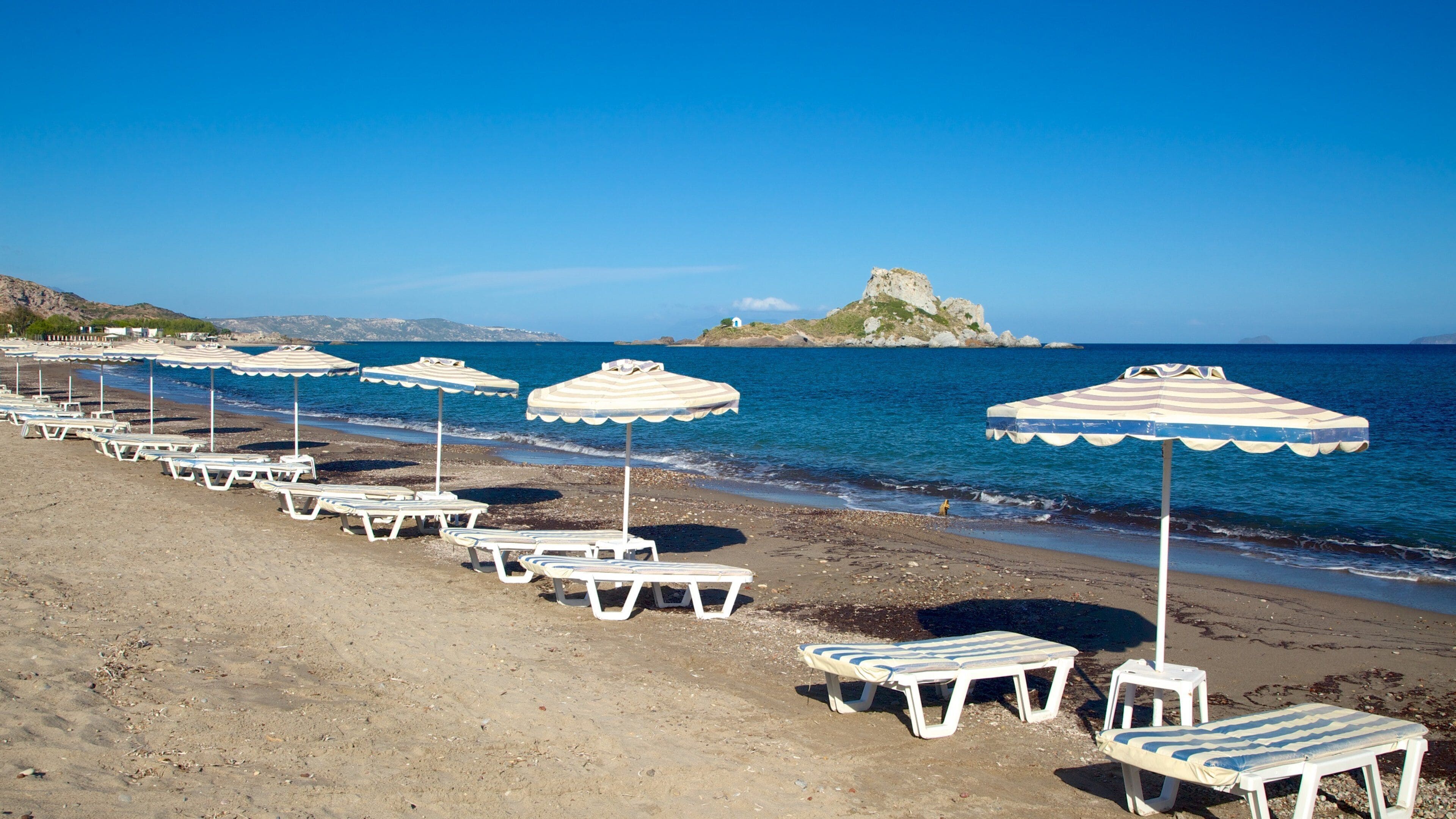 A beach with rows of sun loungers and striped umbrellas.