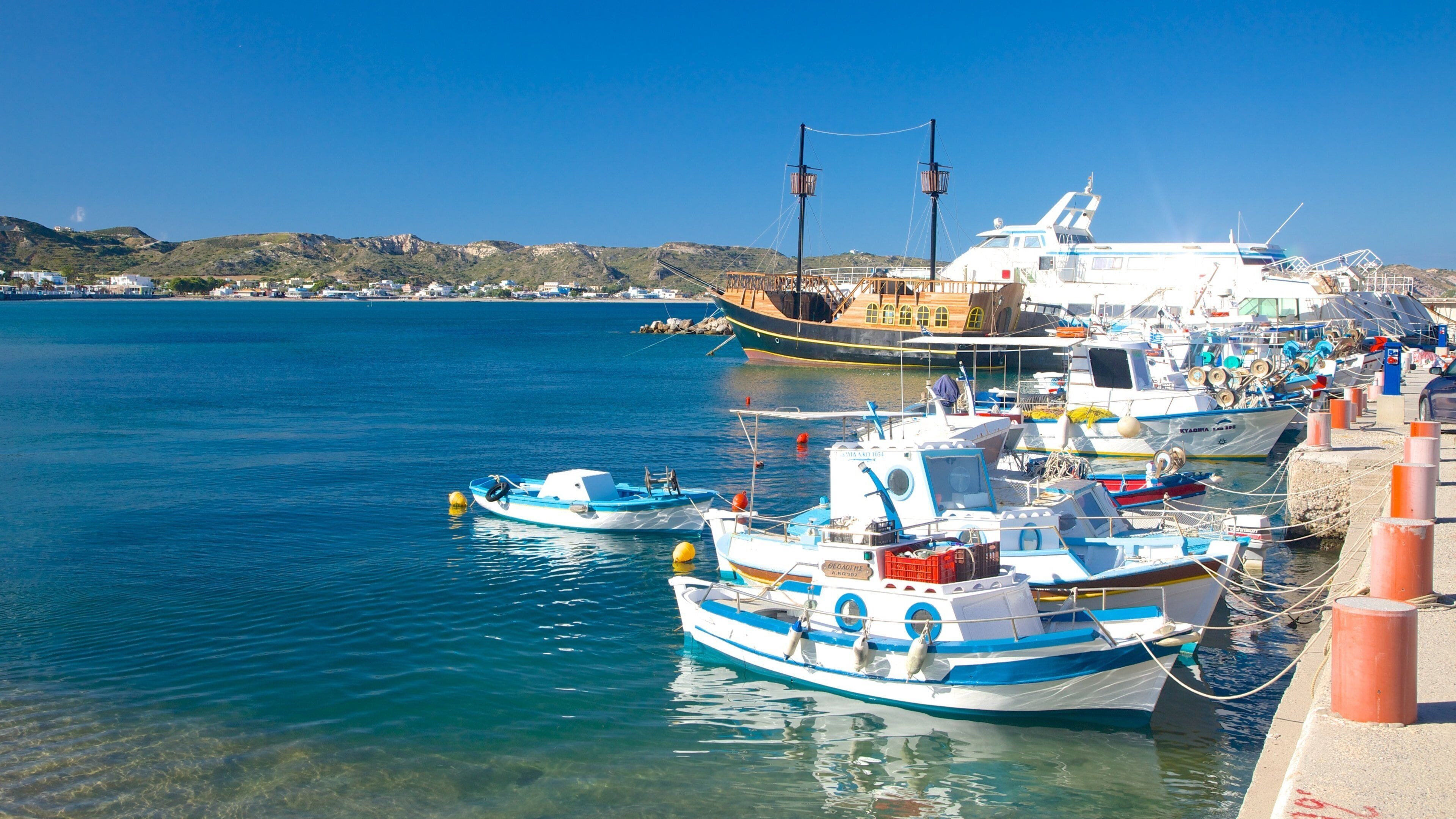 A harbor with several boats docked, a large ship in the background, and a clear blue sky.