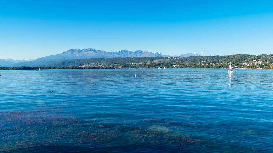 A calm lake with clear water, boats, and mountains in the background.