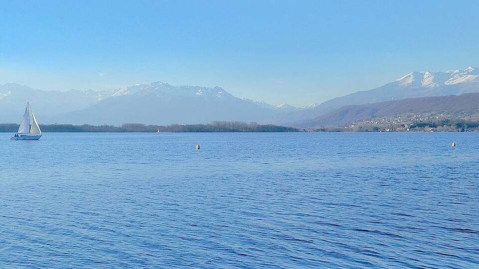 A sailboat on a calm lake with snow-capped mountains in the background.
