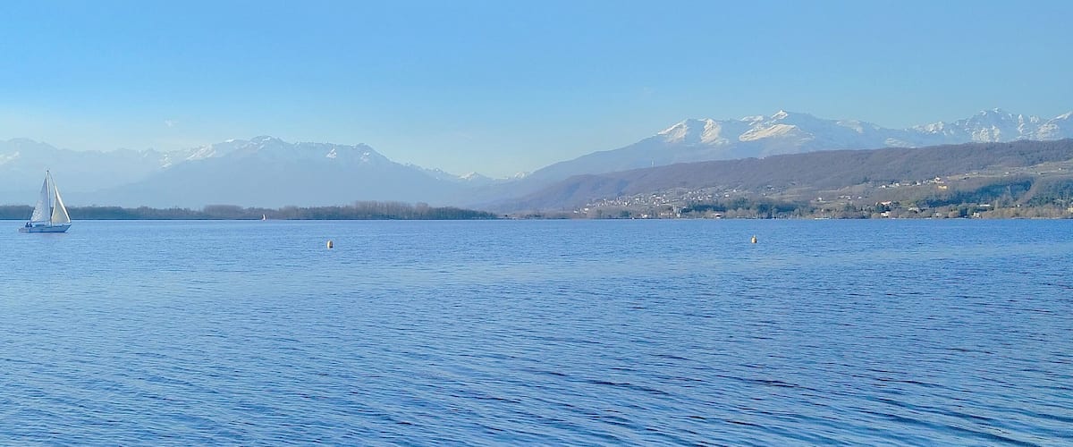 A sailboat on a calm lake with snow-capped mountains in the background.