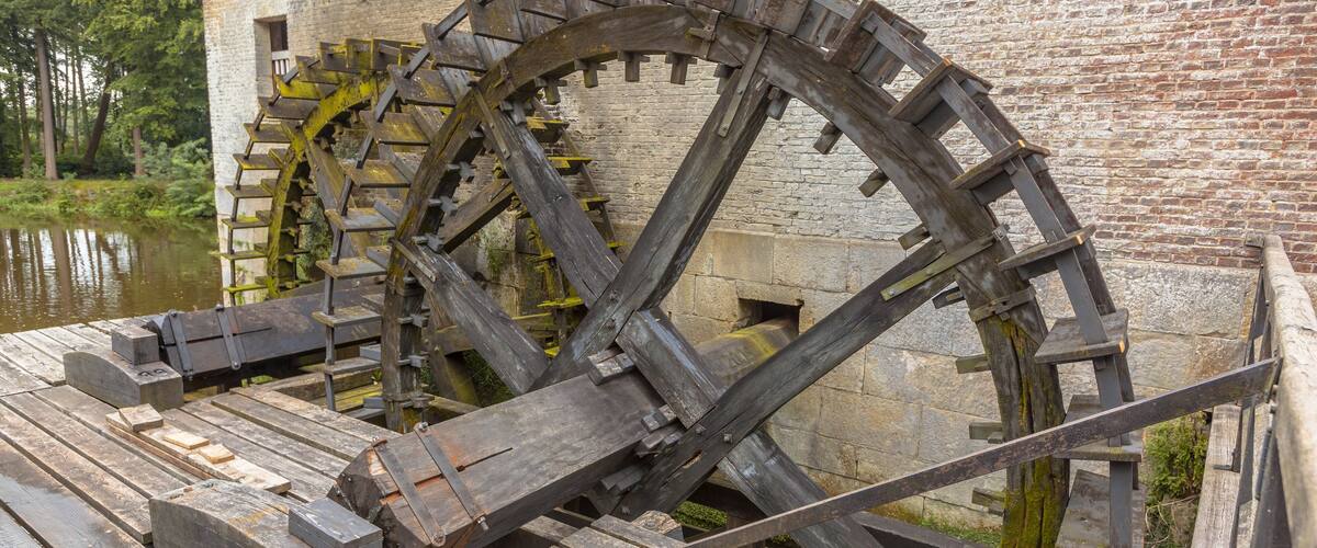 A large wooden water wheel with a brick building in the background.
