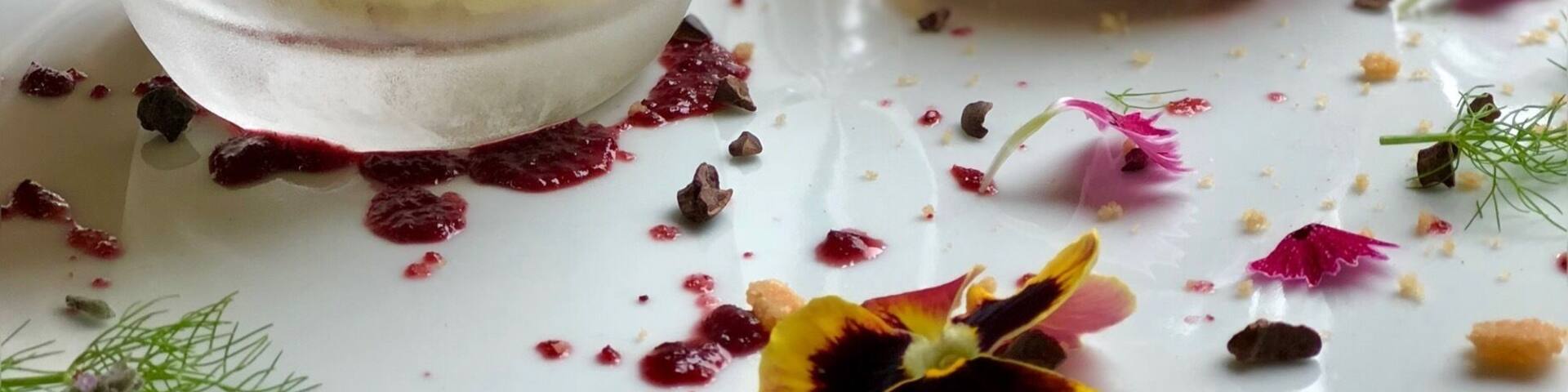 Un postre con capas de crema y frutos rojos, y una bola de helado rosa sobre un plato.