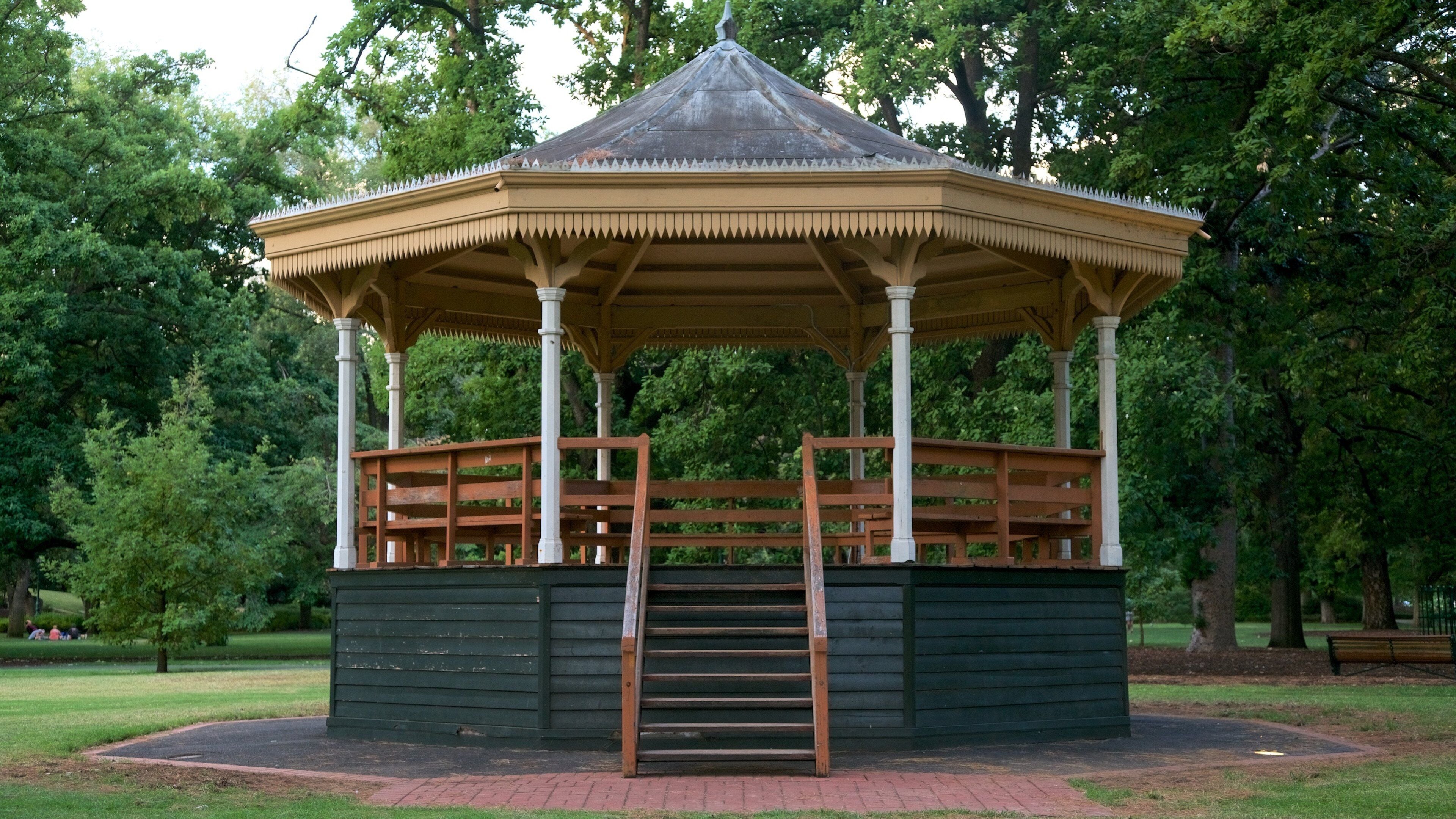 A gazebo with a tiled roof and wooden benches in a park.