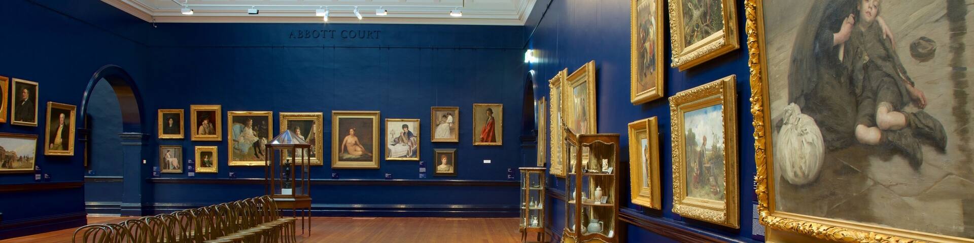 Una galería de arte con suelos de madera, paredes azules y luces en el techo.