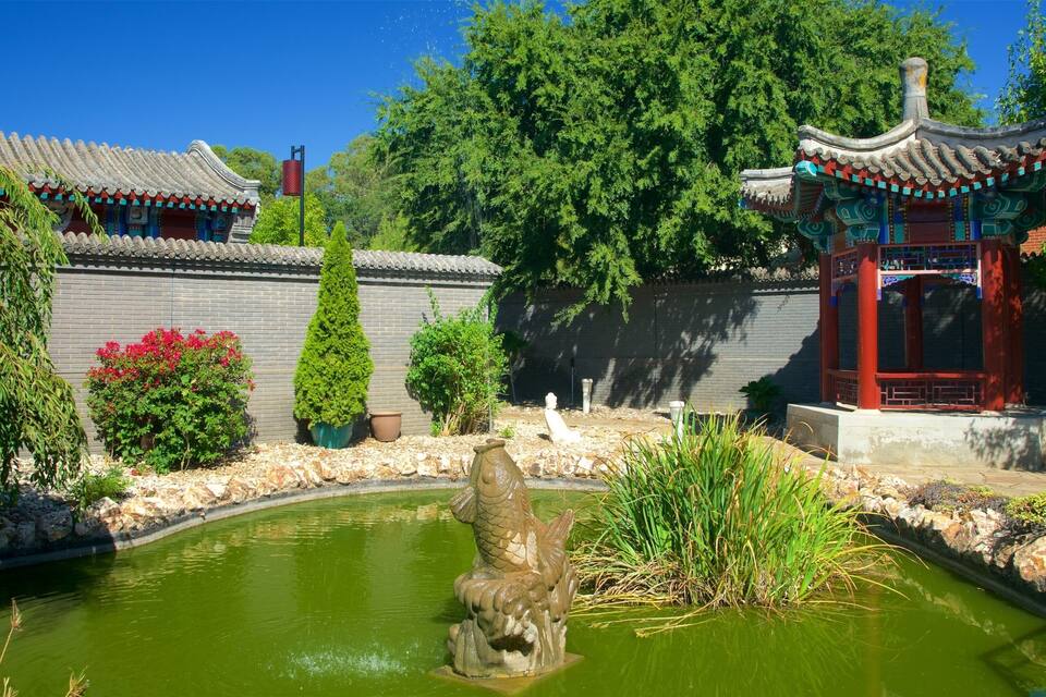 A traditional Chinese garden with a pond, a stone lion statue, and a pagoda.