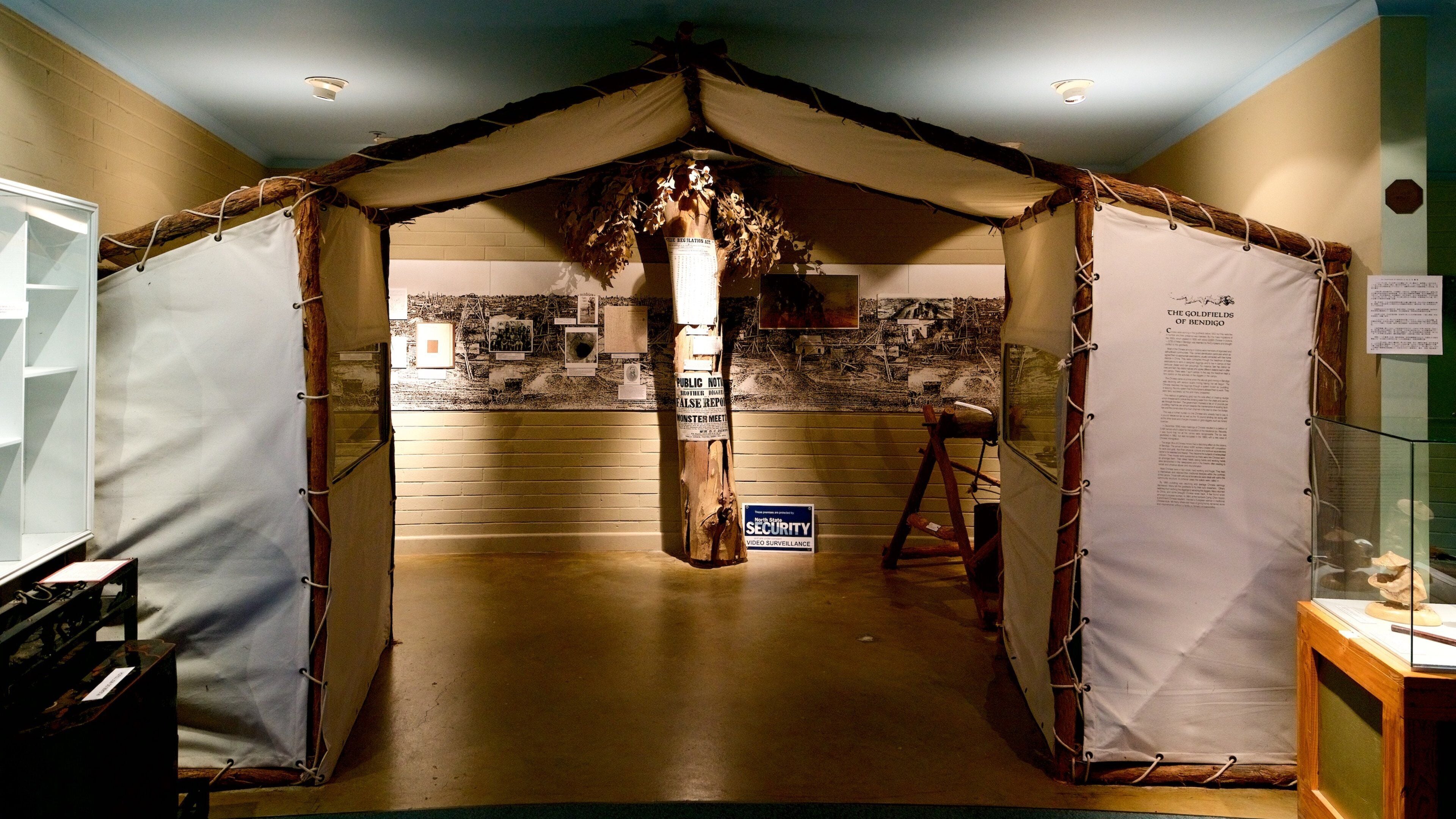 A room with a tent-like structure, a wooden post with a sign, and a display case with a model.