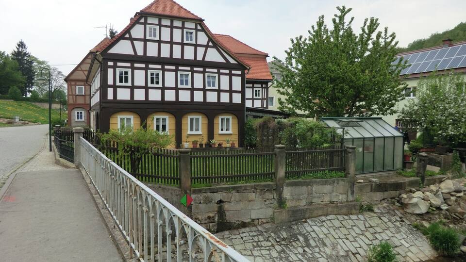 A traditional half-timbered house with a red-tiled roof, a stone wall, and a small stream.