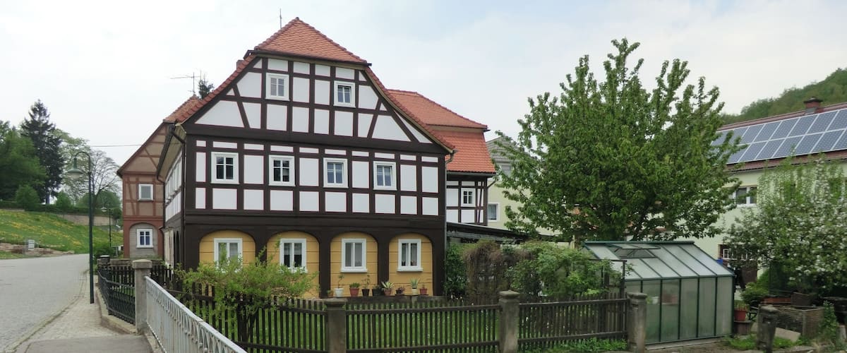 A traditional half-timbered house with a red-tiled roof, a stone wall, and a small stream.