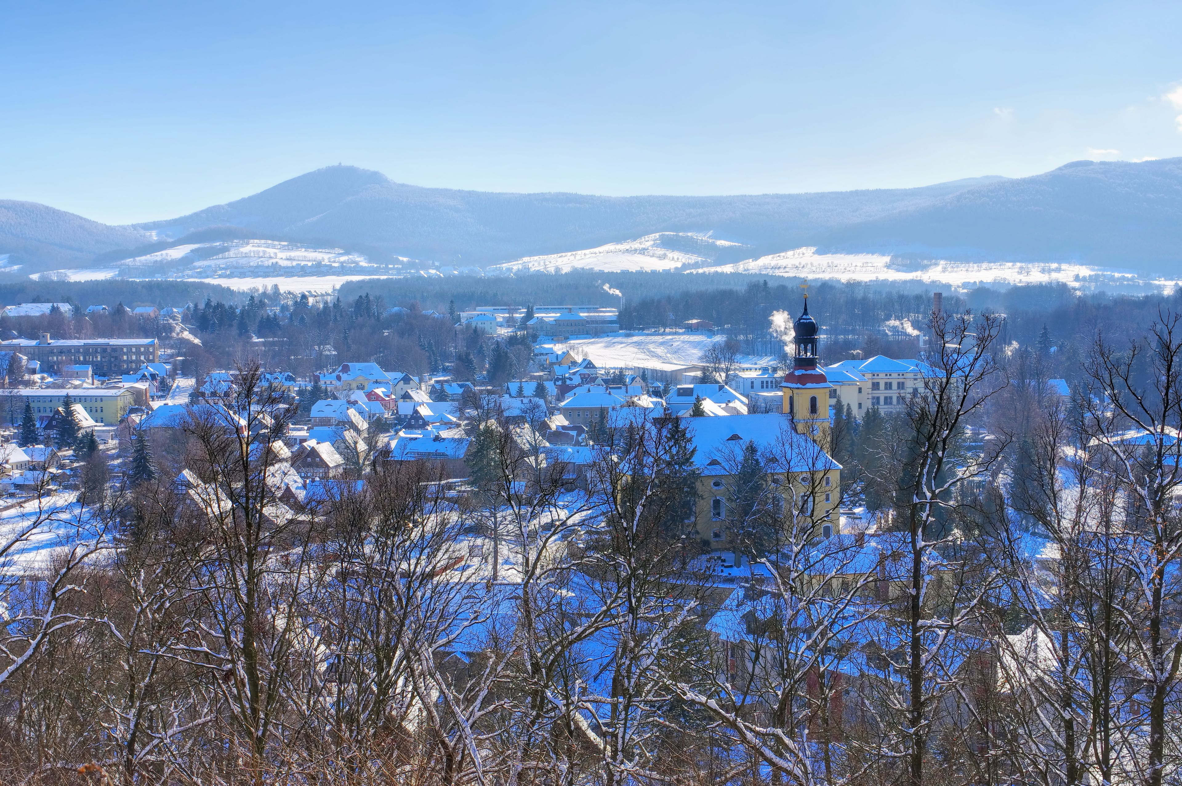 A snow-covered town with a prominent church steeple, surrounded by mountains and trees.