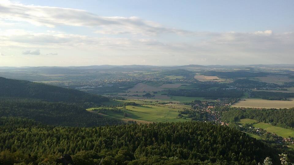 A panoramic view of a valley with dense forests, rolling hills, and a small town in the distance.