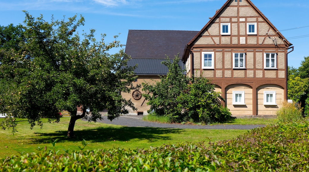 A traditional half-timbered house with a sloped roof, surrounded by lush greenery and trees.
