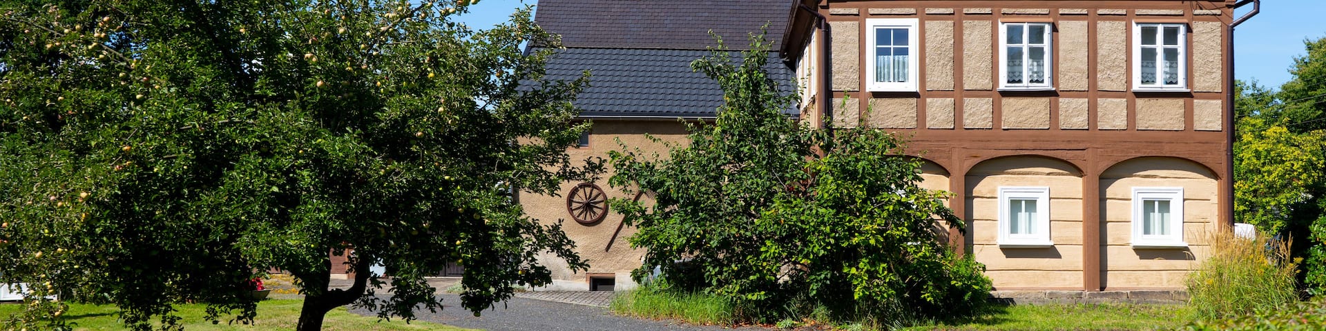A traditional half-timbered house with a sloped roof, surrounded by lush greenery and trees.
