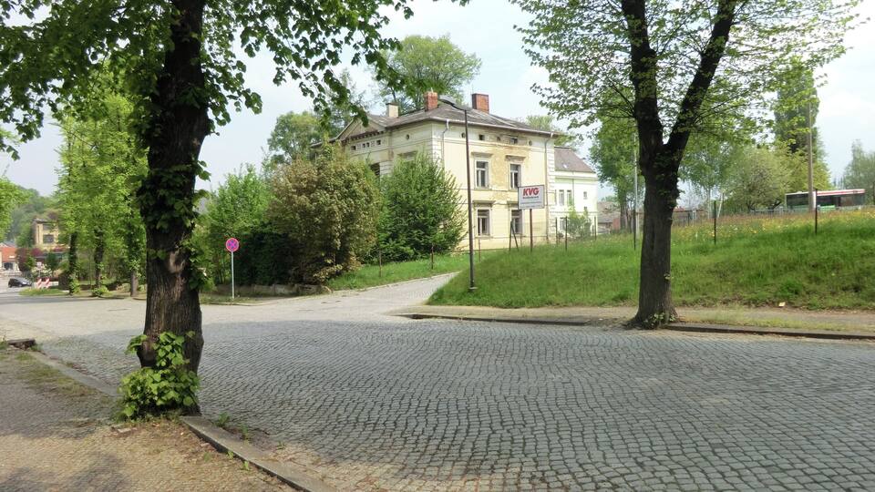 A cobblestone street with trees, a sign for KVG, and a building in the background.
