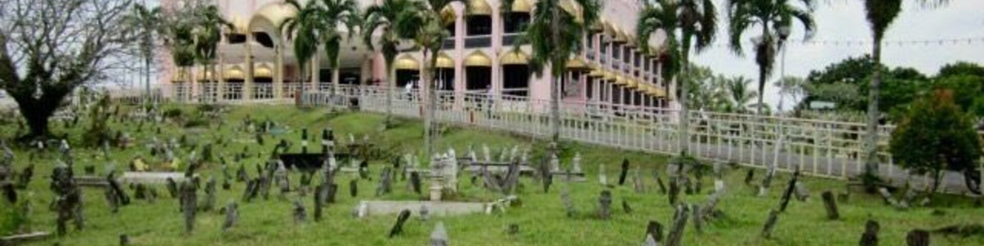 Un edificio grande y ornamentado con cúpulas doradas y torres rosadas, rodeado por un cementerio con numerosas lápidas.