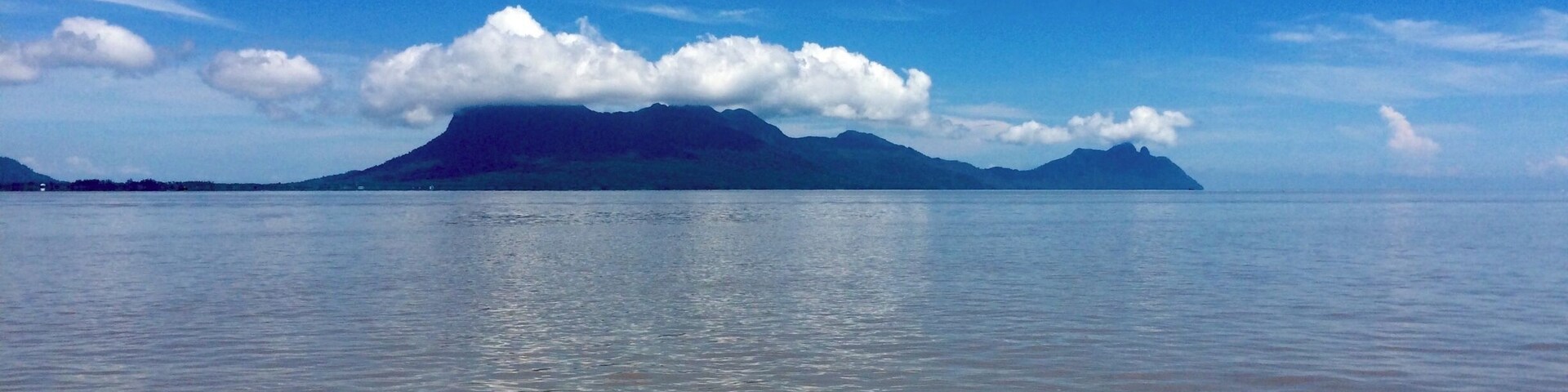 Mar calmo com uma cordilheira distante sob um céu claro.