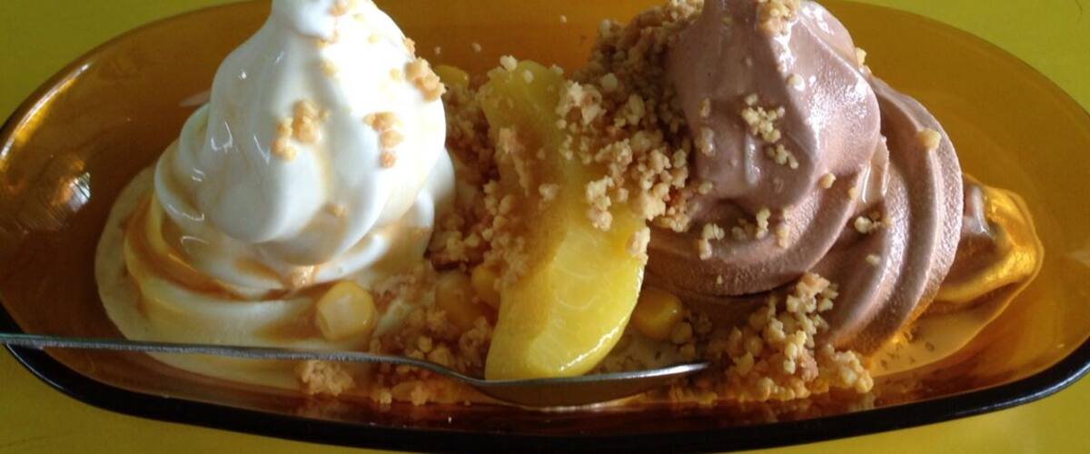 A dessert plate with ice cream and fruit on a yellow table.
