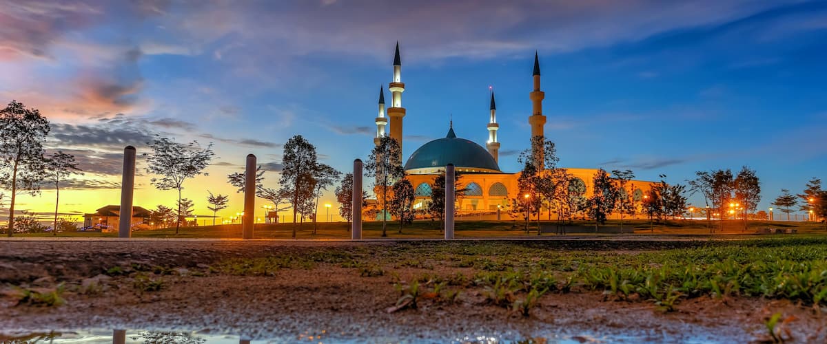 A mosque with a large dome and four minarets, surrounded by trees and a reflective water surface.