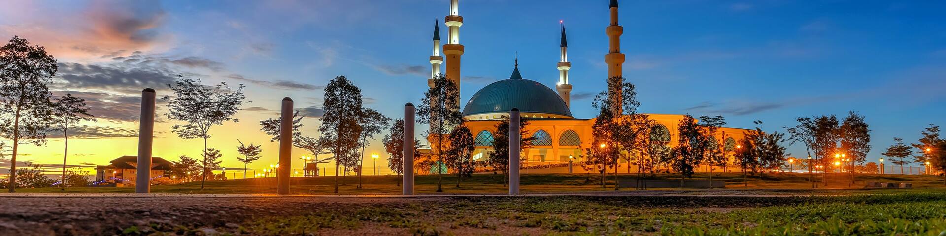 A mosque with a large dome and four minarets, surrounded by trees and a reflective water surface.