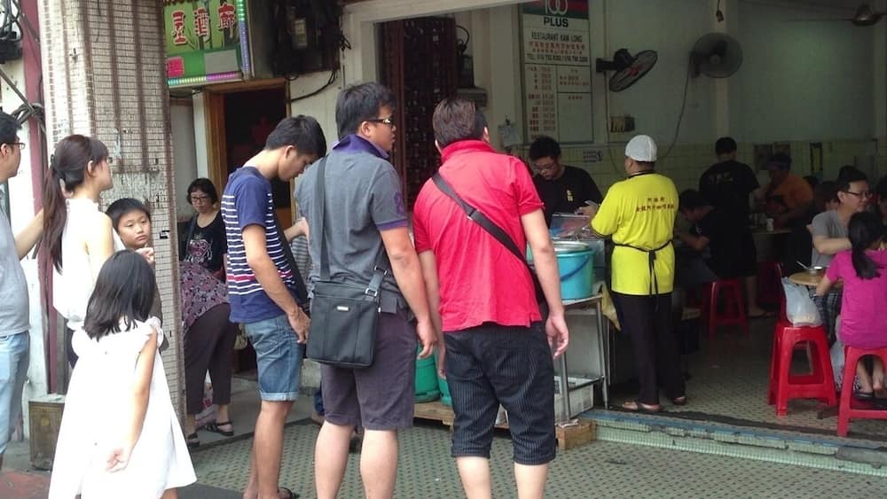 Une file de personnes se tient devant un restaurant dont l’enseigne rouge porte l’inscription « Jasmine ».