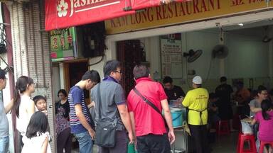 A line of people outside a restaurant with a red sign reading "Jasmine".