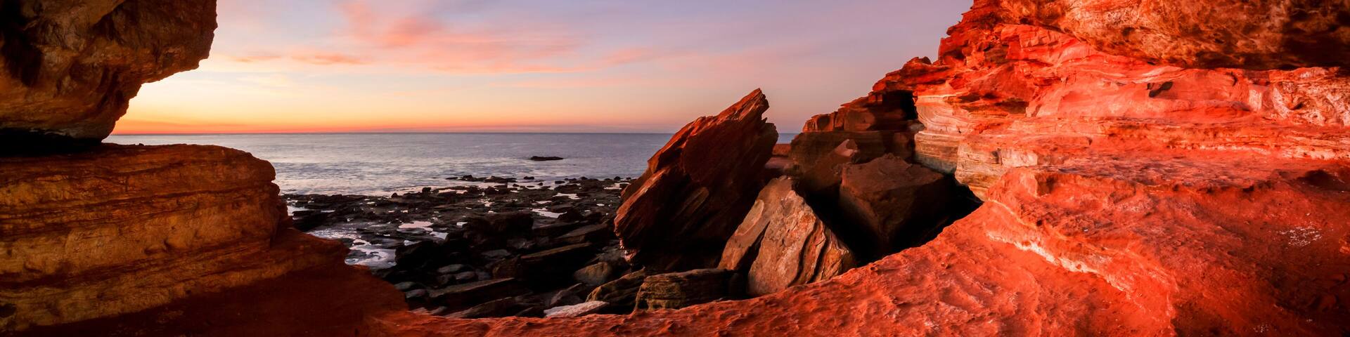 A rock arch formation with a view of the ocean at sunset.