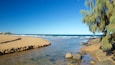 Une plage avec une eau claire, des rochers et un arbre sur la droite.
