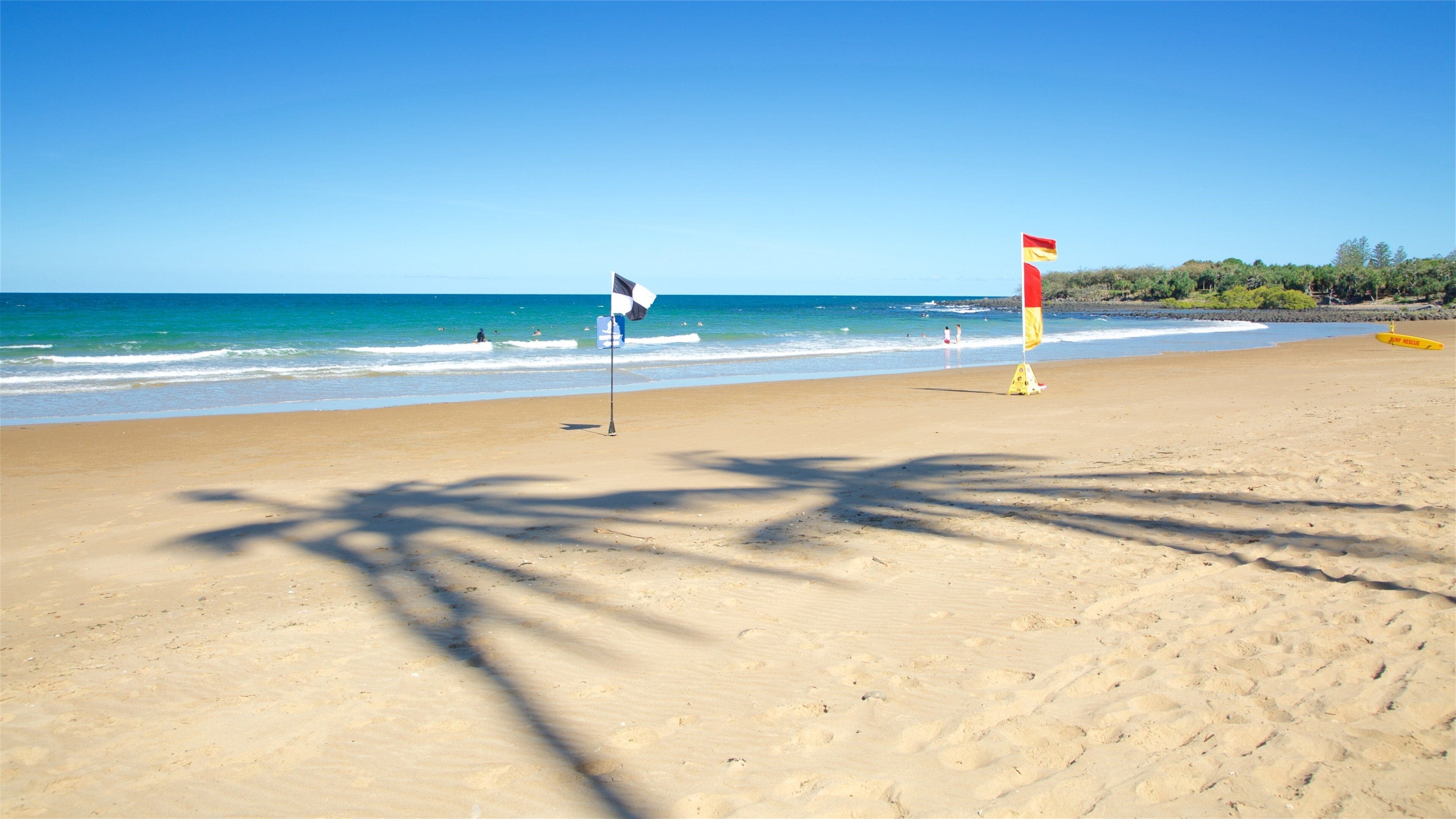 A beach with clear skies, calm waves, and a lifeguard flag.