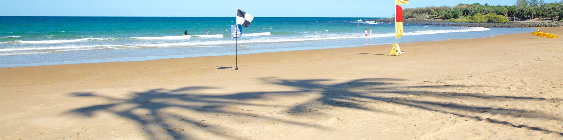 A beach with clear skies, calm waves, and a lifeguard flag.