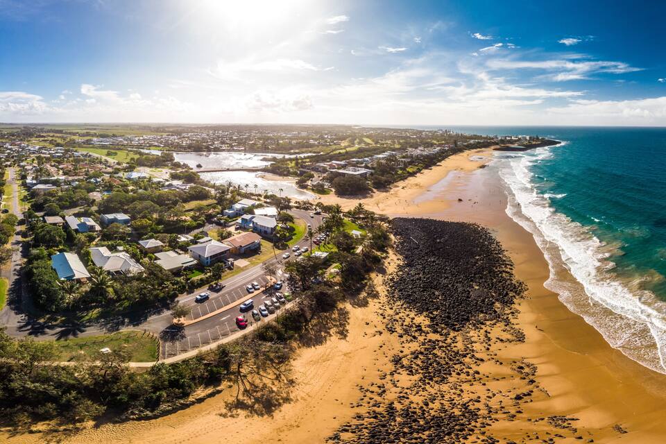 An aerial view of a coastal town with a beach, ocean, and residential area.