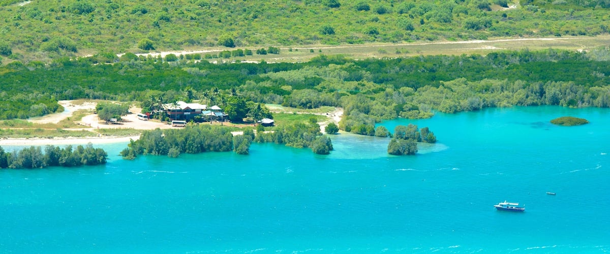 A coastal area with a large body of turquoise water, a small island with dense greenery, and a few buildings near the shore.