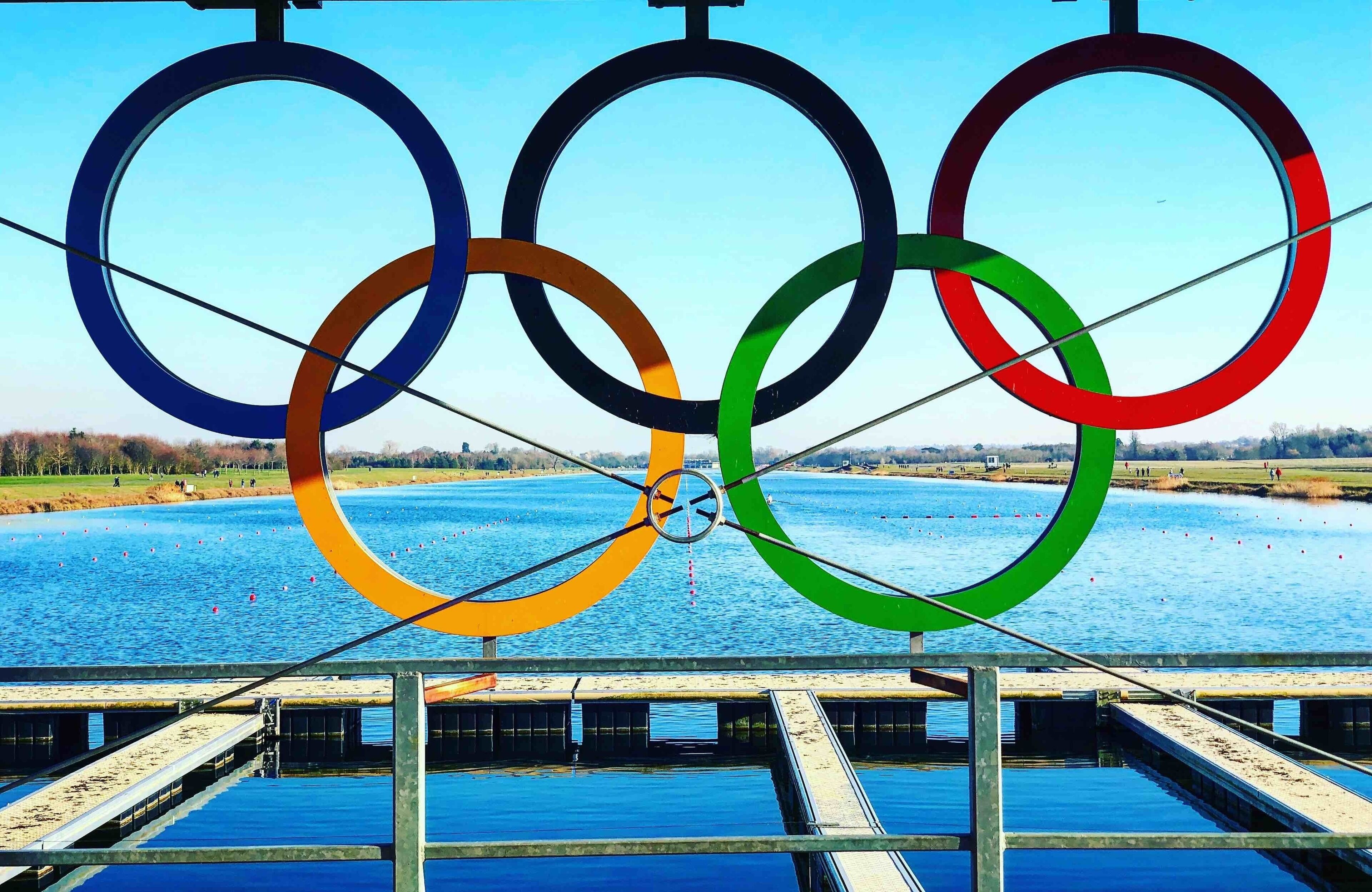 Olympic rings over a river with a bridge in the foreground.