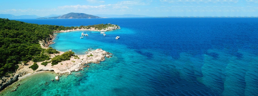 A coastal landscape with clear turquoise waters, rocky shores, and a mountainous backdrop.