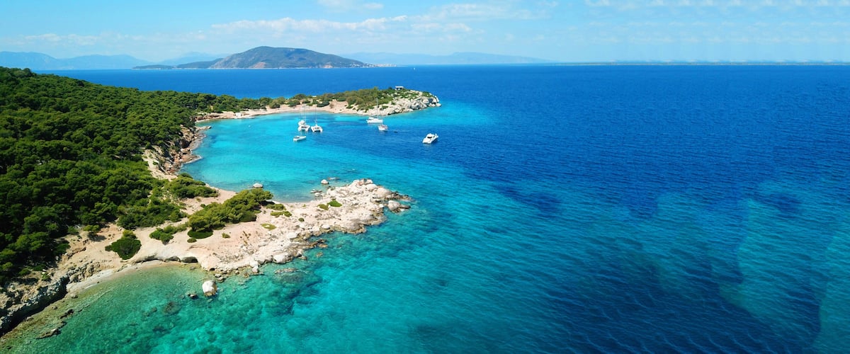 A coastal landscape with clear turquoise waters, rocky shores, and a mountainous backdrop.