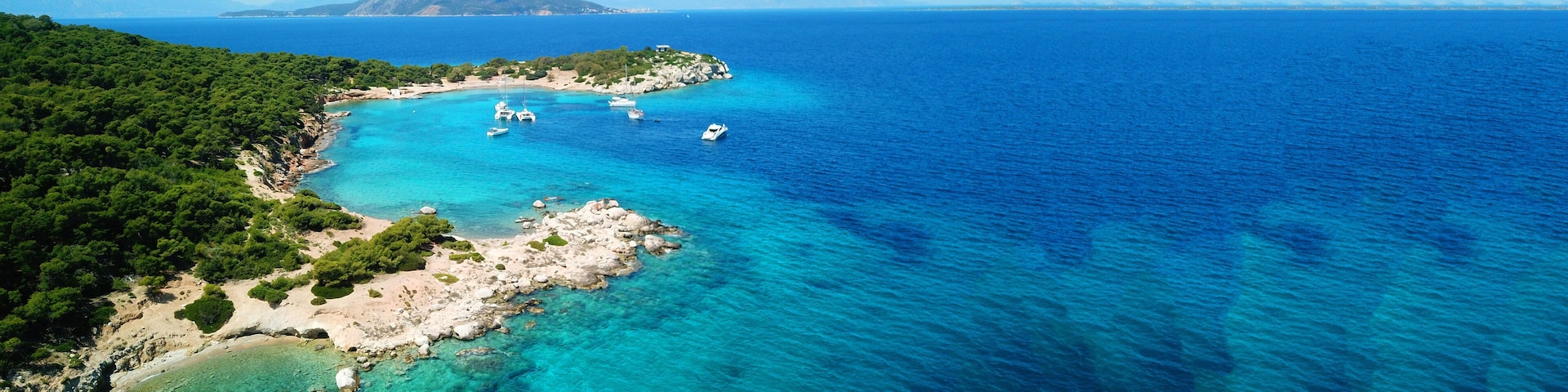 A coastal landscape with clear turquoise waters, rocky shores, and a mountainous backdrop.