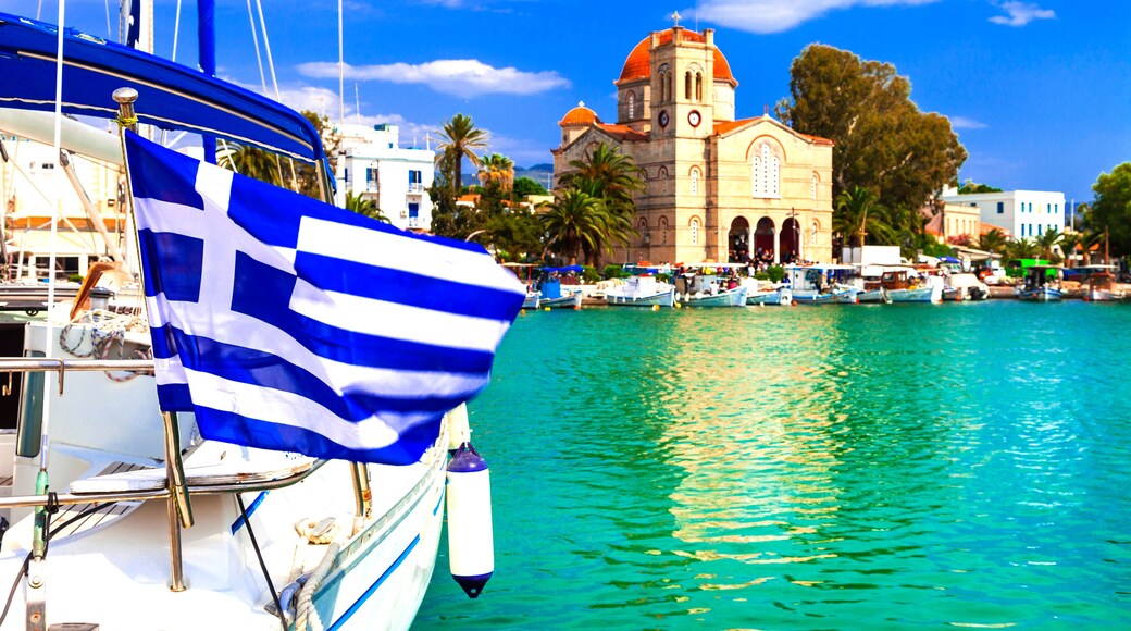 Cinematic View of Aegina Island Harbor — Greek National Flag Waving Over Luxury Yachts and Orthodox Church, Saronic Gulf Port Greece