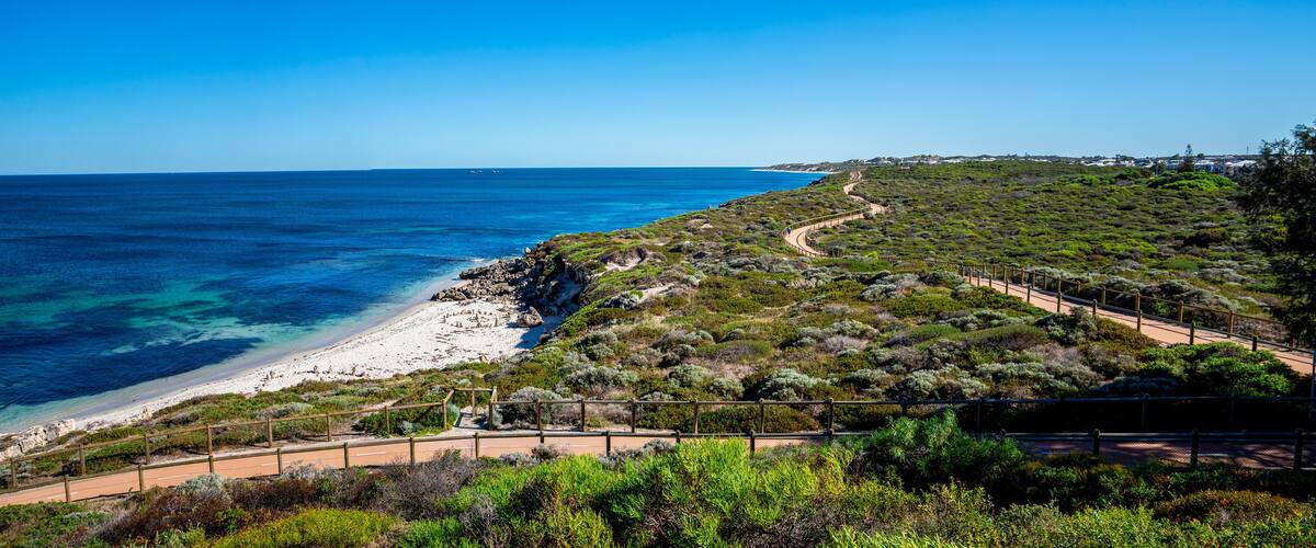 A coastal landscape with a winding road, a sandy beach, and dense shrubbery.