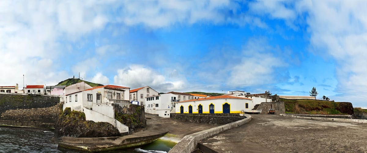 A coastal town with white buildings, a stone wall, and a rocky shoreline.