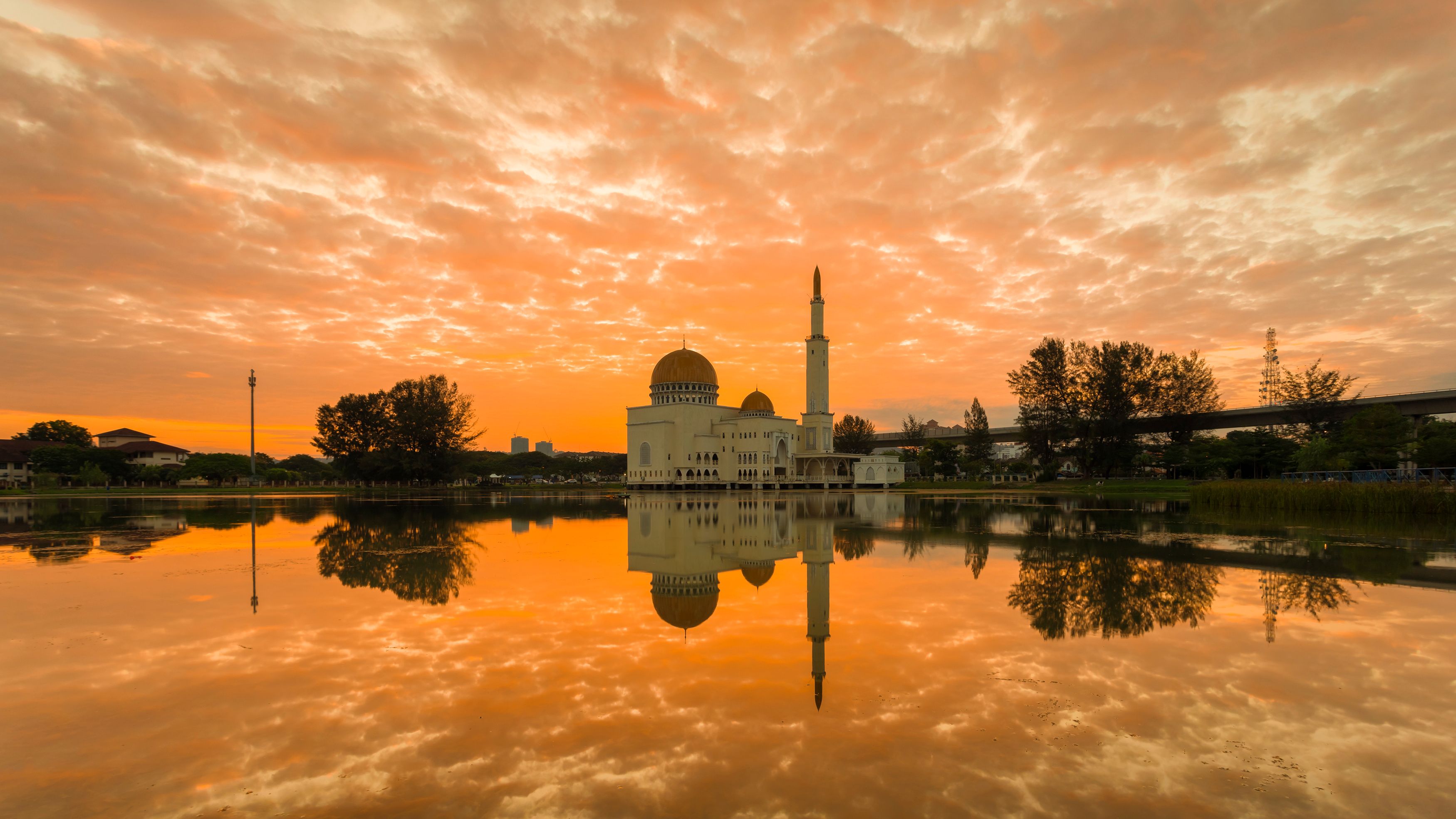 Una mezquita con un minarete alto y una cúpula, reflejada en aguas tranquilas, con un cielo de atardecer al fondo.