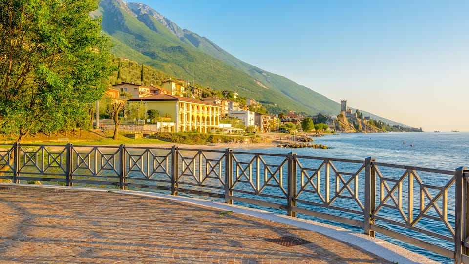 A coastal town with a castle on a hill, a paved walkway, and a body of water.