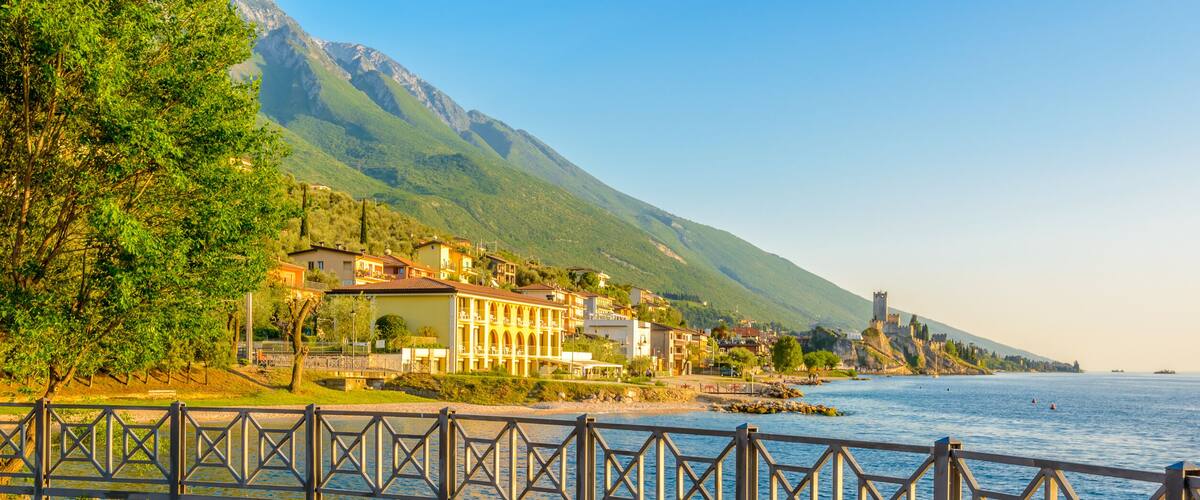 A coastal town with a castle on a hill, a paved walkway, and a body of water.