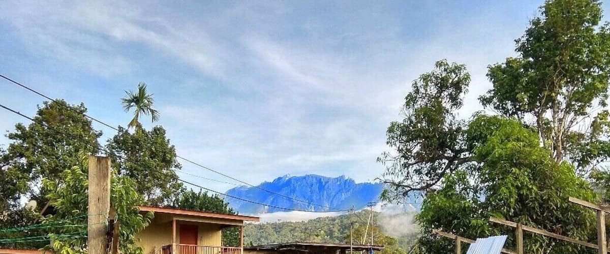 A rural setting with a fenced area containing chickens, a parked car, and a mountain in the background.