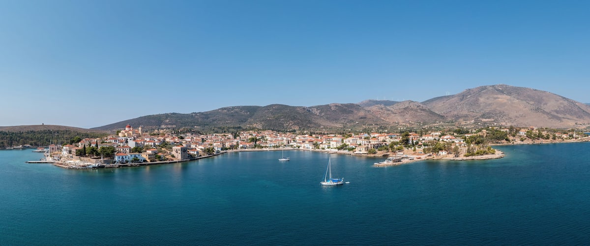A coastal town with a marina, surrounded by mountains and a clear blue sea.