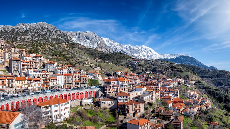 A mountainous town with red-roofed buildings and a snow-capped peak in the background.