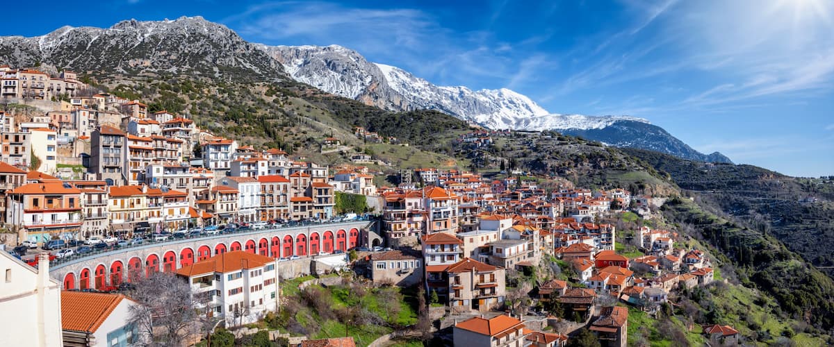 A mountainous town with red-roofed buildings and a snow-capped peak in the background.