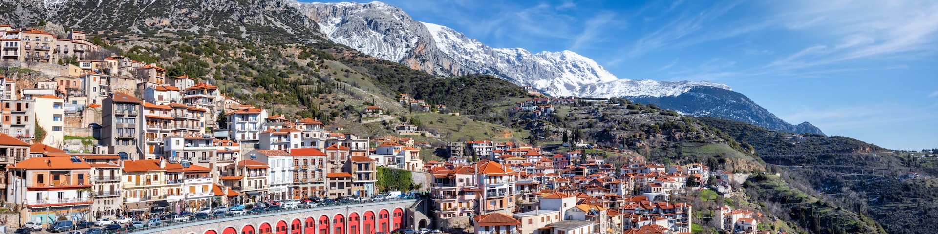 A mountainous town with red-roofed buildings and a snow-capped peak in the background.