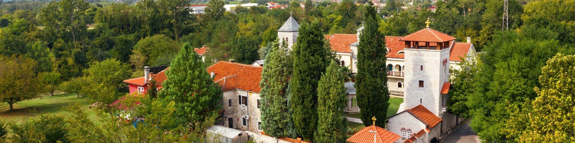 A historic monastery complex with red-tiled roofs, surrounded by lush greenery and a mountain backdrop.