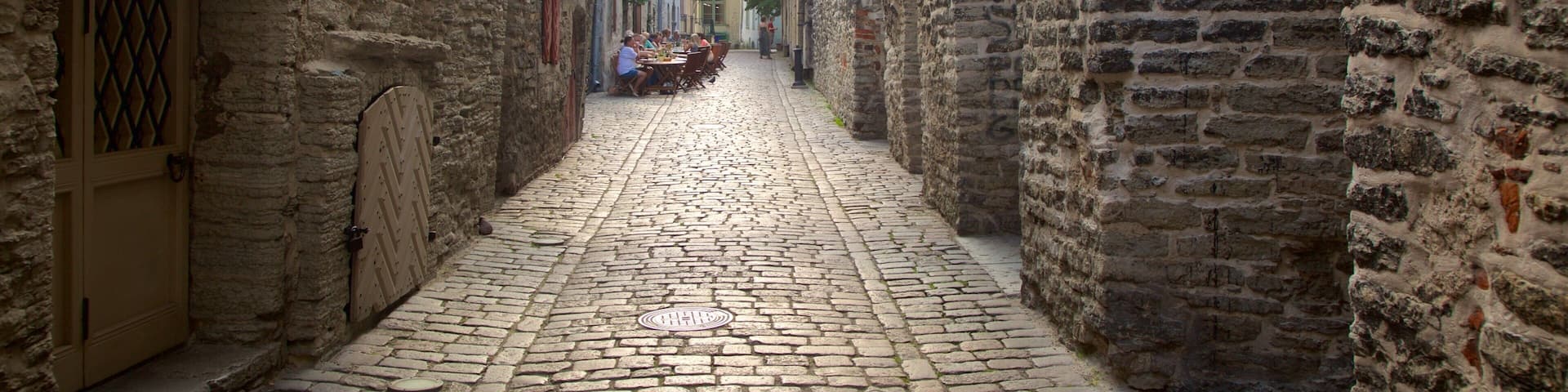 A cobblestone alleyway with stone walls, a tiled roof, and a clock.
