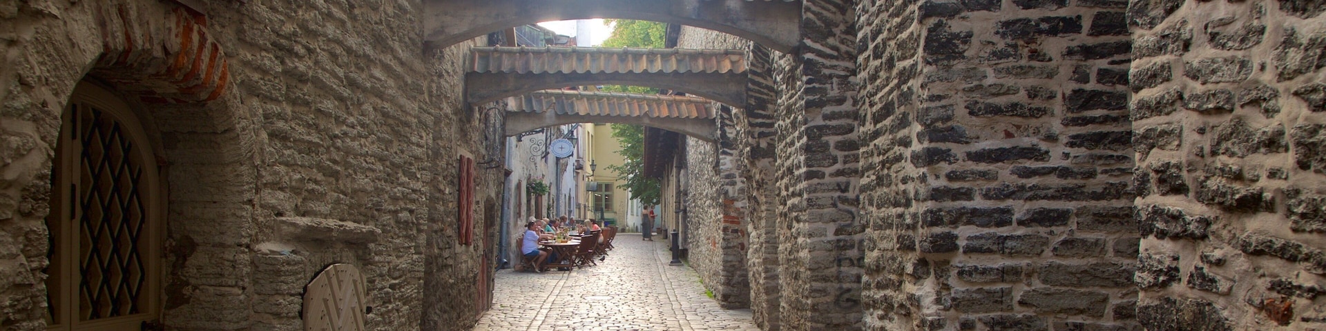 Un callejón empedrado con muros de piedra, techo de tejas y un reloj.